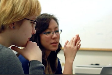 Two women sit next to each other and look at a screen just out of view.