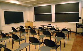 Four rows of tablet armchairs facing sliding chalkboards at front and side of room. An instructor’s table is in front of the chalkboards.