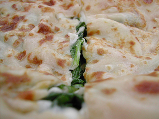 A very think pancake and a pile of spinach sit on a white plate.