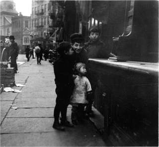 Black and white photo of two girls and two boys, standing in front of a shoeshine stand.