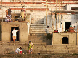 Women washing clothes, men gathered in groups, a flight of stairs ascending up from the riverbank.