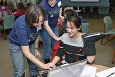 A girl is holding a boot with wires on it. An adult volunteer is helping her.